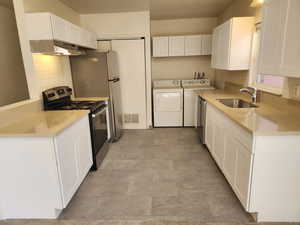 Kitchen with visible vents, stainless steel appliances, under cabinet range hood, a sink, and washing machine and dryer