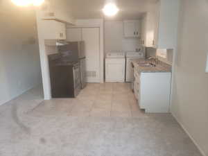 Kitchen featuring washing machine and clothes dryer, visible vents, white cabinets, and a sink