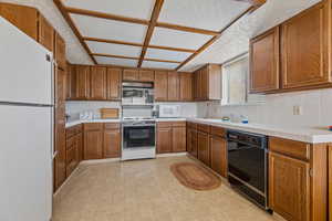 Kitchen with brown cabinetry, white appliances, tile counters, a sink, and backsplash