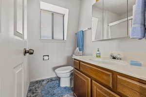 Full bath featuring vanity, baseboards, a shower with door, and toilet