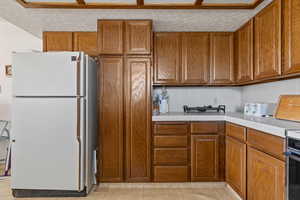 Kitchen featuring decorative backsplash, freestanding refrigerator, brown cabinetry, and tile counters