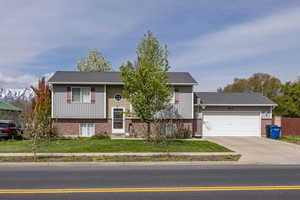 Split-entry with fence, an attached garage, brick siding, a front yard, and concrete driveway