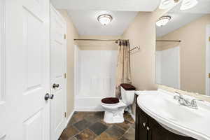 Full bathroom featuring vanity, toilet, a textured ceiling, stone tile floors, and baseboards