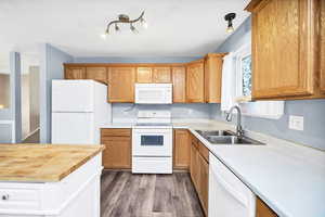 Kitchen with a sink, laminate countertops, island with butcher block countertop, white appliances, and dark wood-style floors
