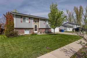 Split foyer home featuring a garage, driveway, a front lawn, and brick siding