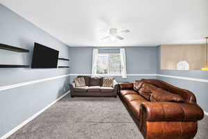 Carpeted living room featuring a ceiling fan and baseboards