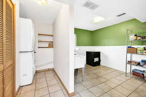 Interior space with light tile patterned floors, a wainscoted wall, stacked washer / drying machine, and visible vents