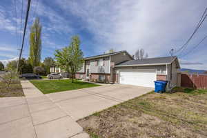 View of front of property featuring fence, brick siding, a garage, a front yard, and driveway