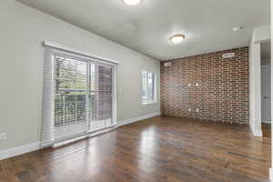 Empty room with visible vents, baseboards, wood finished floors, and brick wall