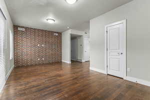 Empty room featuring a textured ceiling, brick wall, baseboards, wood finished floors, and visible vents
