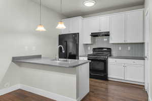 Kitchen with a sink, dark wood finished floors, tasteful backsplash, under cabinet range hood, and black appliances
