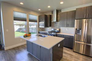 Kitchen featuring wall chimney range hood, appliances with stainless steel finishes, a sink, baseboards, and light countertops