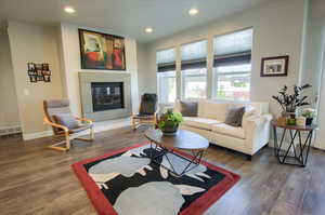 Living room with a glass covered fireplace, baseboards, recessed lighting, and wood finished floors