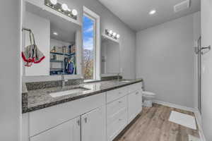 Full bathroom featuring double vanity, visible vents, wood finished floors, a sink, and toilet