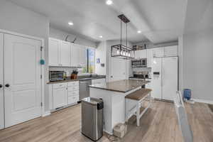 Kitchen featuring a center island, white cabinetry, a sink, light wood finished floors, and stainless steel appliances