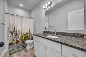 Bathroom with vanity, toilet, shower / bath combination with curtain, recessed lighting, and wood finished floors