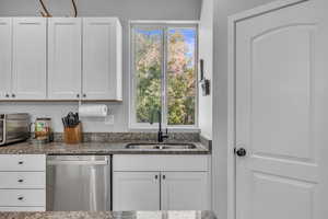 Kitchen featuring stainless steel dishwasher, white cabinets, a sink, and dark stone countertops