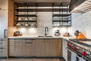 Kitchen with wall chimney range hood, decorative backsplash, high end stainless steel range oven, and a sink