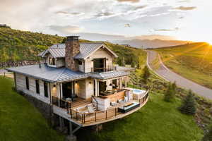 Back of house with a balcony, a standing seam roof, metal roof, a lawn, and an in ground hot tub