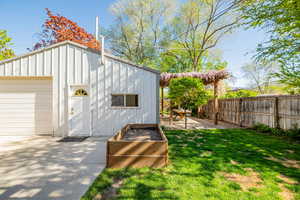 Back yard showing grass area, wisteria covered outdoor entertaining space, oversized detached garage, and large garden box with drip irrigation.