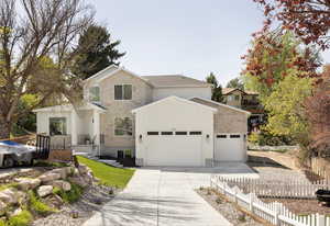 Traditional-style house featuring an attached garage, fence, driveway, and stone siding