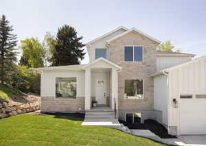View of front of property featuring a garage, board and batten siding, a front lawn, and stone siding