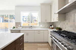 Kitchen with wall chimney range hood, light wood-type flooring, light countertops, a sink, and appliances with stainless steel finishes