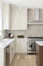 Kitchen with stainless steel appliances, light wood finished floors, a sink, and wall chimney exhaust hood