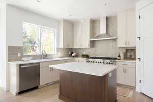 Kitchen with light countertops, wall chimney exhaust hood, a sink, light wood-style flooring, and dishwasher