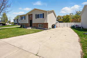 View of front of property with brick siding, fence, a front yard, and concrete driveway