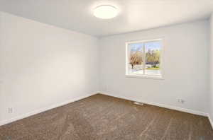 Spare room featuring dark carpet, baseboards, and visible vents