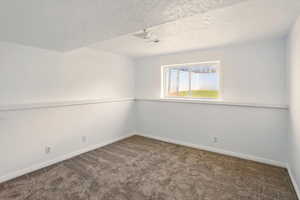 Empty room with baseboards, carpet, and a textured ceiling
