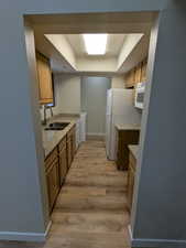 Kitchen featuring brown cabinets, a sink, a raised ceiling, white appliances, and light wood-style flooring