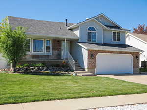 Split level home featuring concrete driveway, a porch, a front yard, and a garage