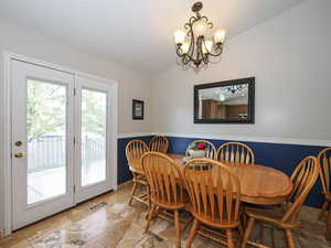 Dining space with visible vents, stone tile flooring, lofted ceiling, a wainscoted wall, and a chandelier