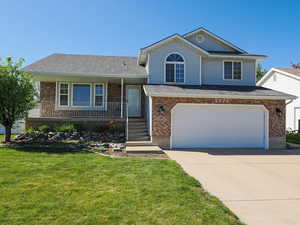 Tri-level home featuring covered porch, driveway, brick siding, and a front yard