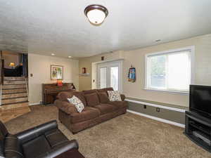 Carpeted living room featuring baseboards, a textured ceiling, stairs, and visible vents