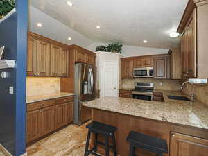 Kitchen with a peninsula, lofted ceiling, light stone countertops, a sink, and stainless steel appliances