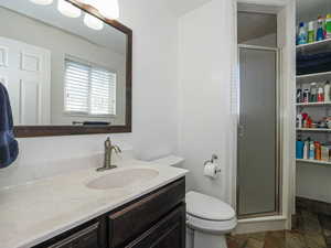 Full bath with vanity, a stall shower, toilet, and stone tile flooring