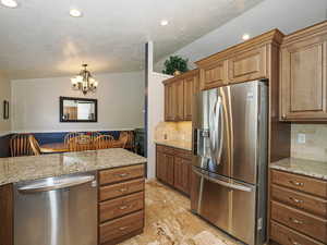 Kitchen featuring brown cabinets, stainless steel appliances, a notable chandelier, and backsplash