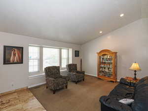 Carpeted living area featuring baseboards, vaulted ceiling, and visible vents