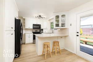 Kitchen with a sink, black appliances, light wood finished floors, a peninsula, and glass insert cabinets