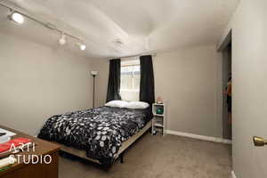 Carpeted bedroom with baseboards, visible vents, and track lighting