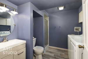 Full bathroom featuring vanity, wood finished floors, washer and dryer, toilet, and a shower stall