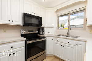Kitchen with black microwave, stainless steel range with electric cooktop, light countertops, a sink, and white cabinetry
