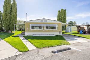 Manufactured / mobile home with a storage unit, an outdoor structure, a front lawn, and a carport