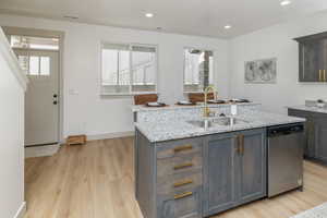 Kitchen featuring a sink, stainless steel dishwasher, light wood-type flooring, and an island with sink