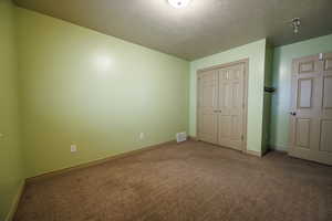 Unfurnished bedroom with visible vents, a closet, baseboards, a textured ceiling, and carpet flooring