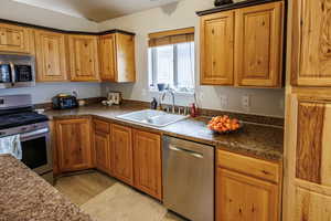 Kitchen featuring a sink, appliances with stainless steel finishes, vaulted ceiling, and dark countertops