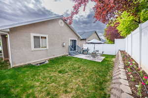 Rear view of property featuring stucco siding, a fenced backyard, entry steps, a lawn, and a patio